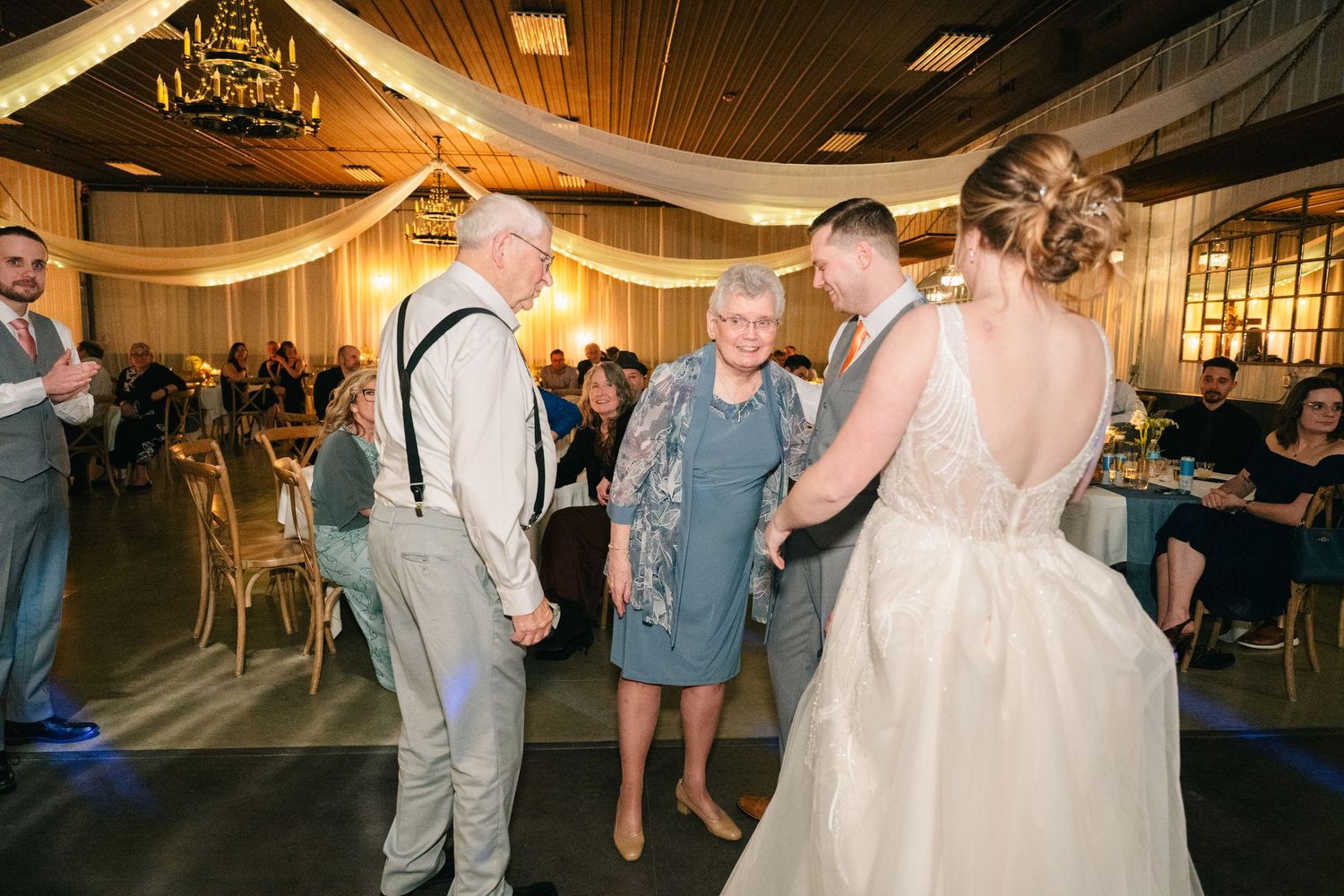 Newlyweds dancing with elderly grandparents on the wedding reception dance floor.