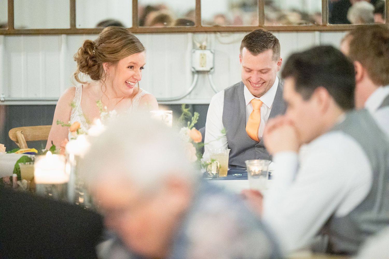 Bride and groom laugh joyfully during wedding reception speeches at a candlelit table.