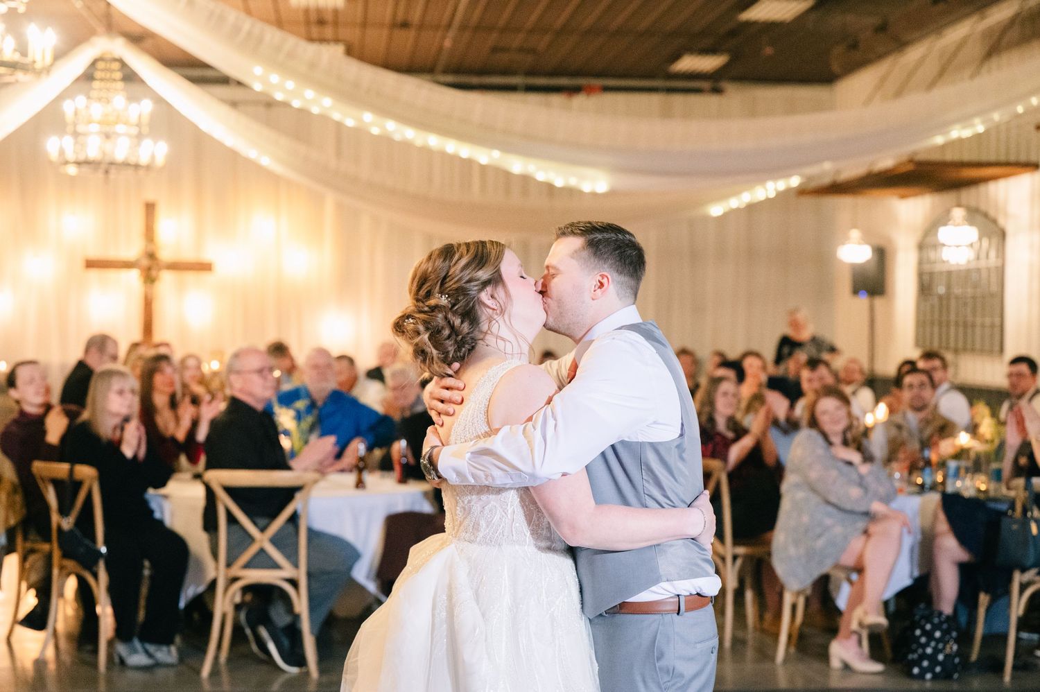 Bride and groom sharing their first kiss on the dance floor surrounded by wedding guests.