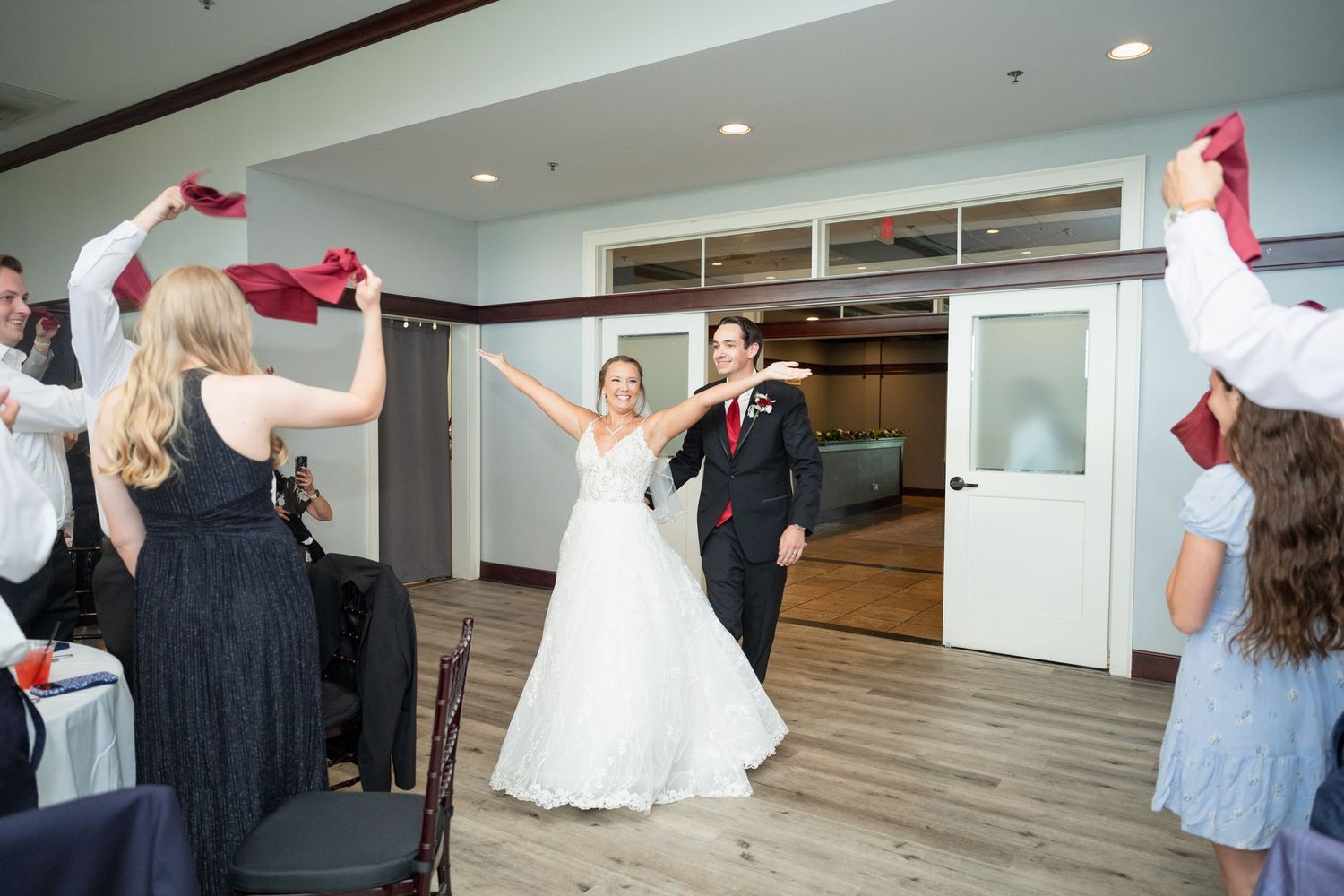 Bride and groom make grand entrance at wedding reception as guests wave red napkins.