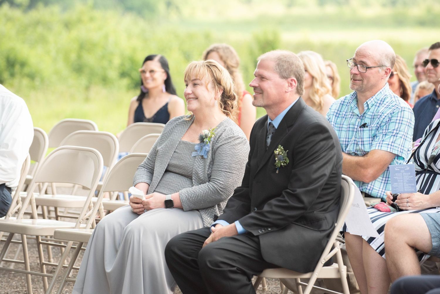 Wedding ceremony guests seated in white chairs on a sunny outdoor lawn. Zimmerman MN Weddings