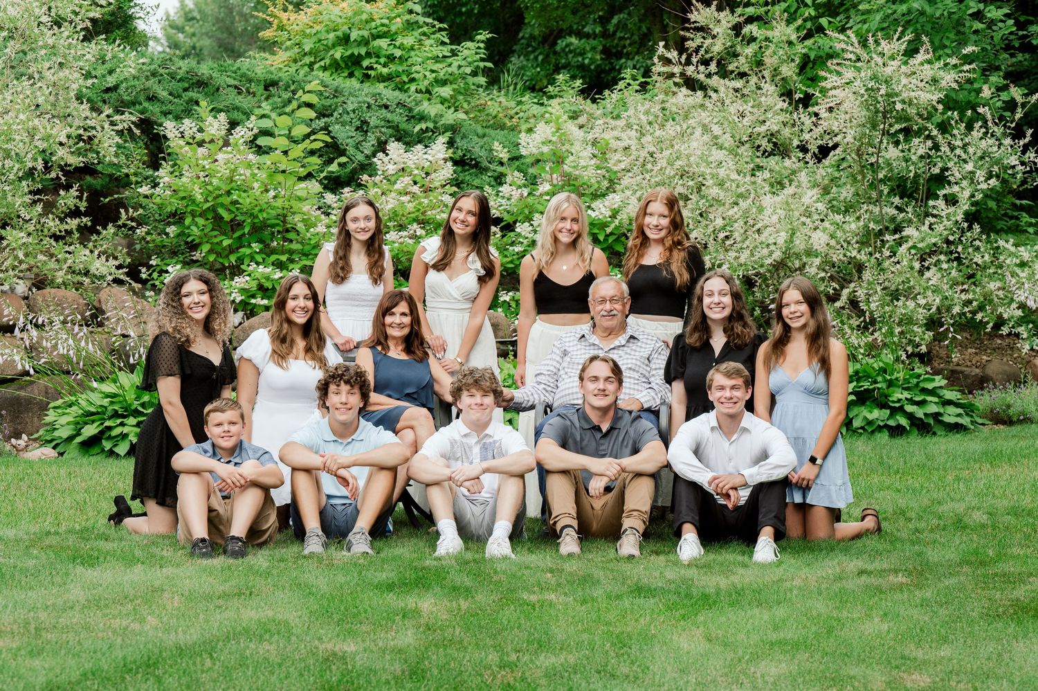 Clear Lake MN Family PLarge family group wearing coordinated white and gray outfits poses together on grass in front of lush garden setting.