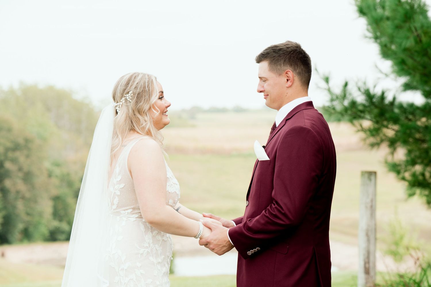 A couple holding hands during their outdoor wedding ceremony with a burgundy suit and white dress.