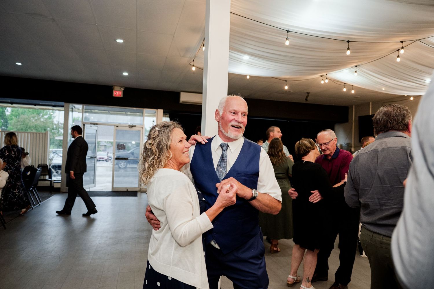 Guests mingling and socializing in an indoor wedding reception venue with track lighting overhead.