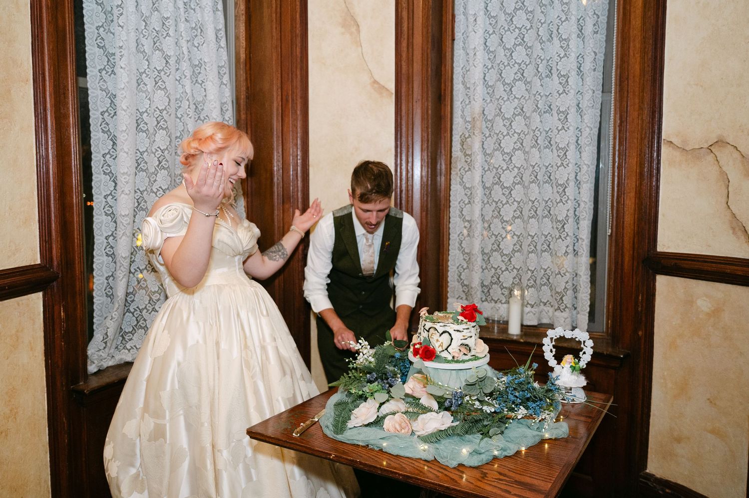 Central MN Wedding Photos | Bride and groom cutting wedding cake decorated with greenery at reception.