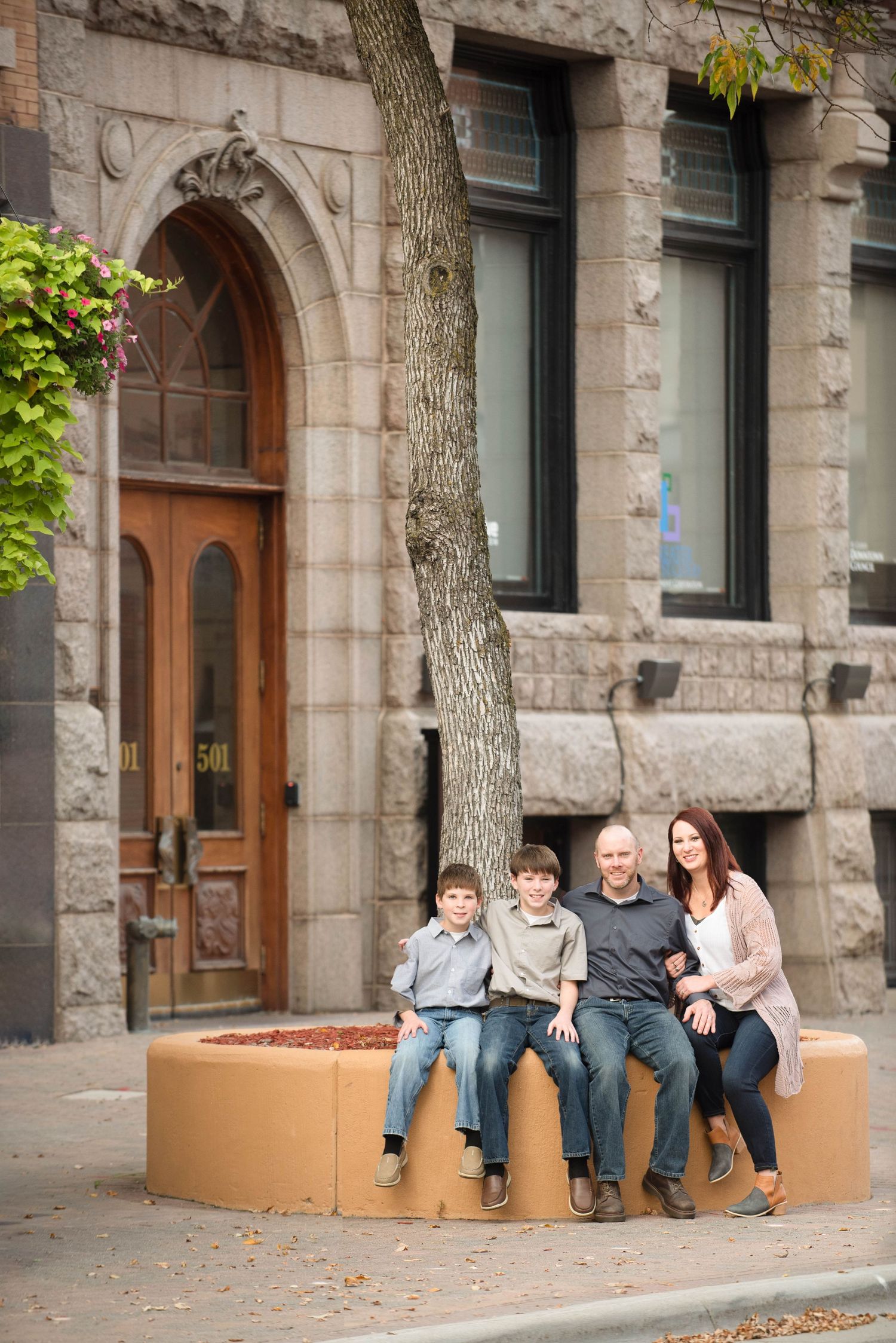 A family sits together on a curved stone bench outside a historic stone building with arched doorways.