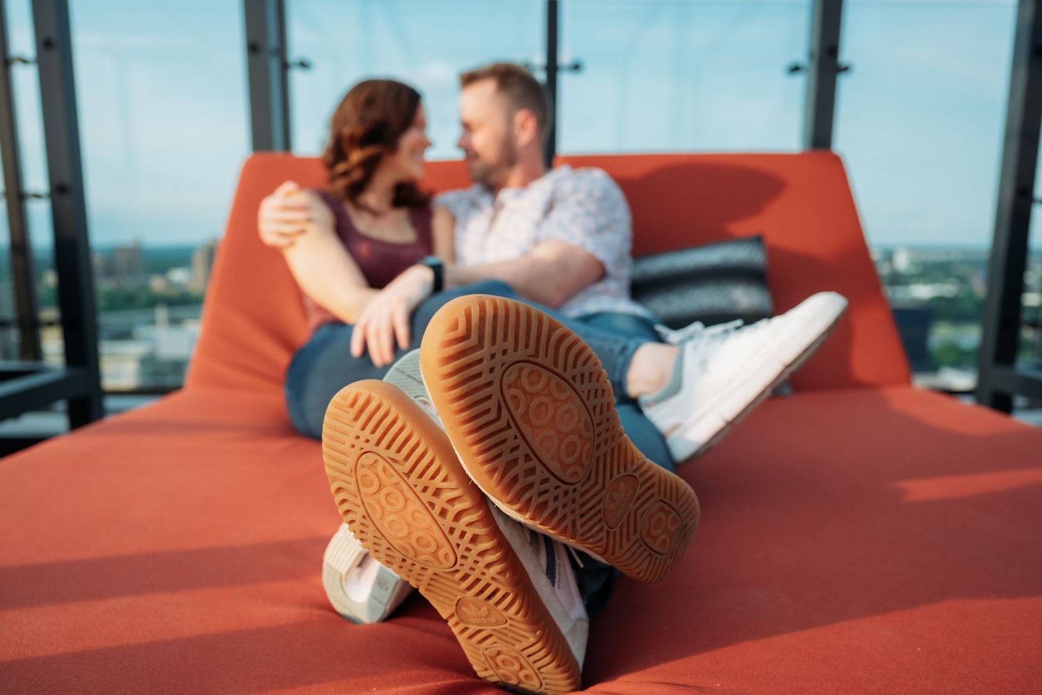 A couple relaxes on orange outdoor furniture on a rooftop lounge area.