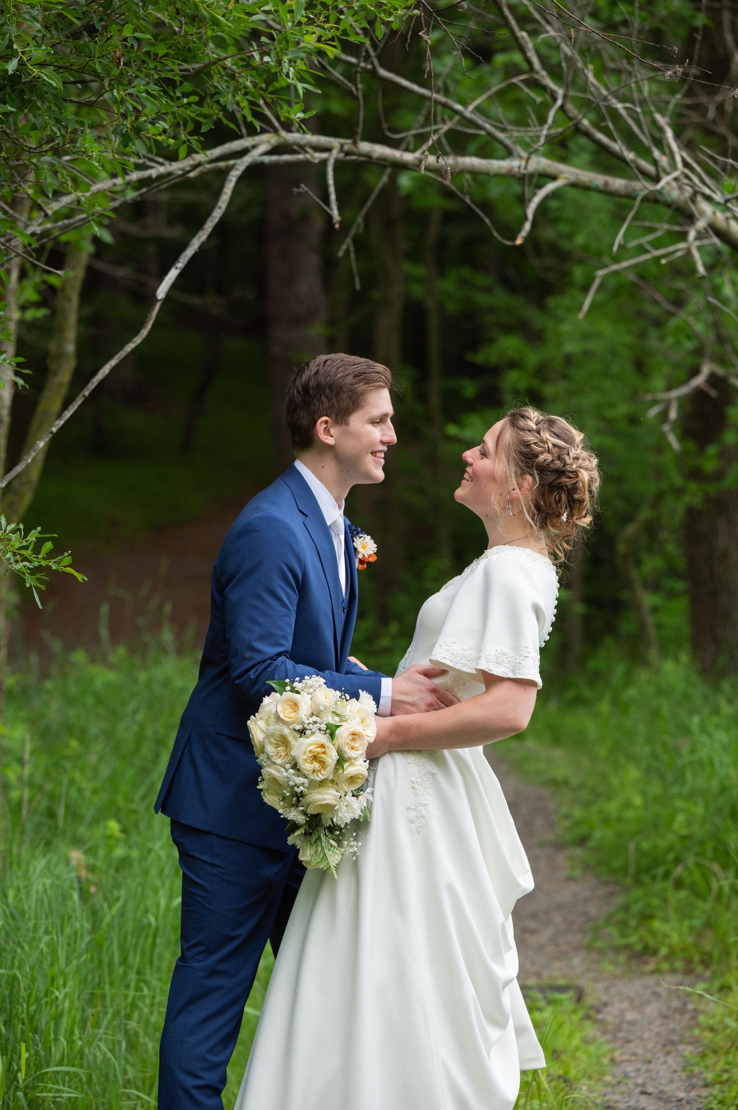 A joyful wedding moment captured on a forest path with white bouquet.