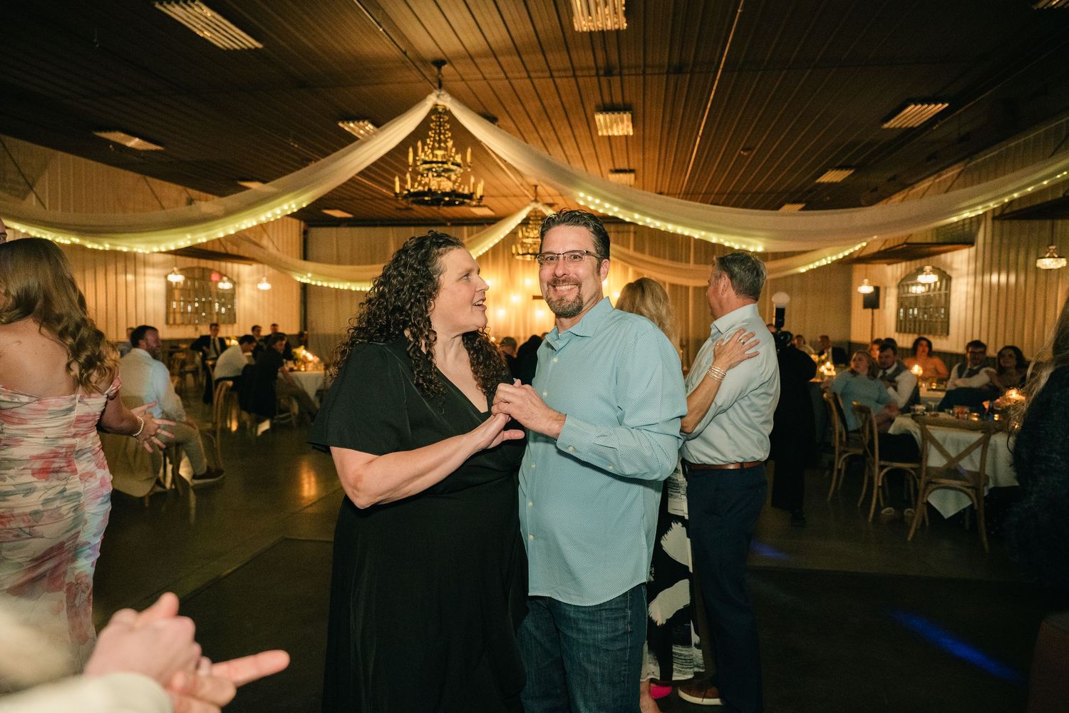 Couple dances joyfully at wedding reception in decorated banquet hall with string lights.