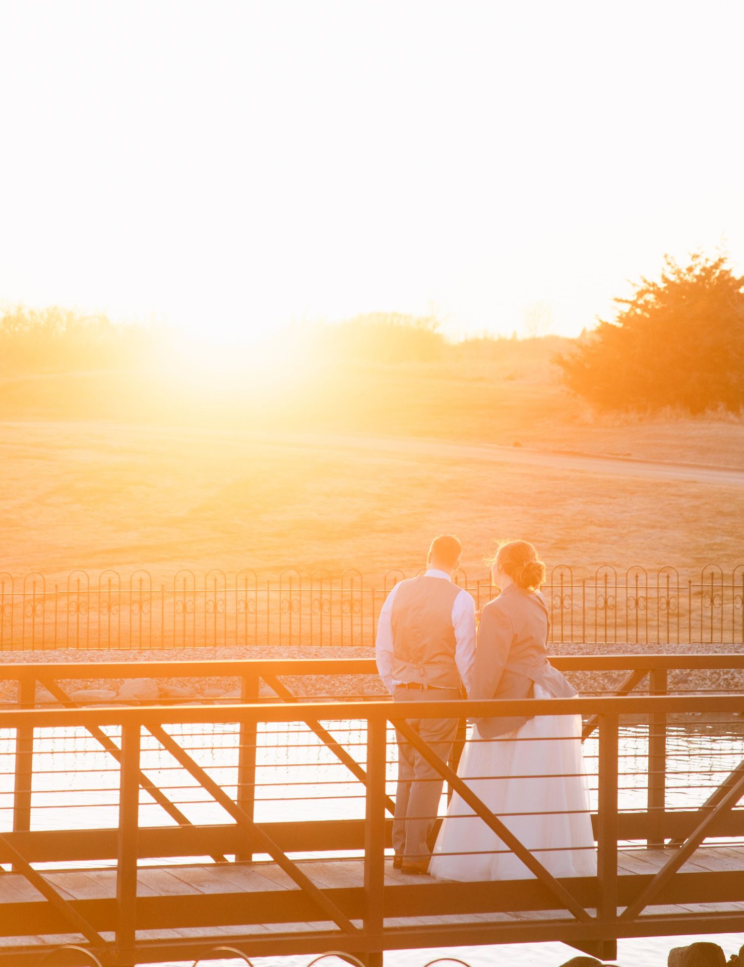Bride and groom share a romantic sunset moment on a bridge overlooking a golden landscape.