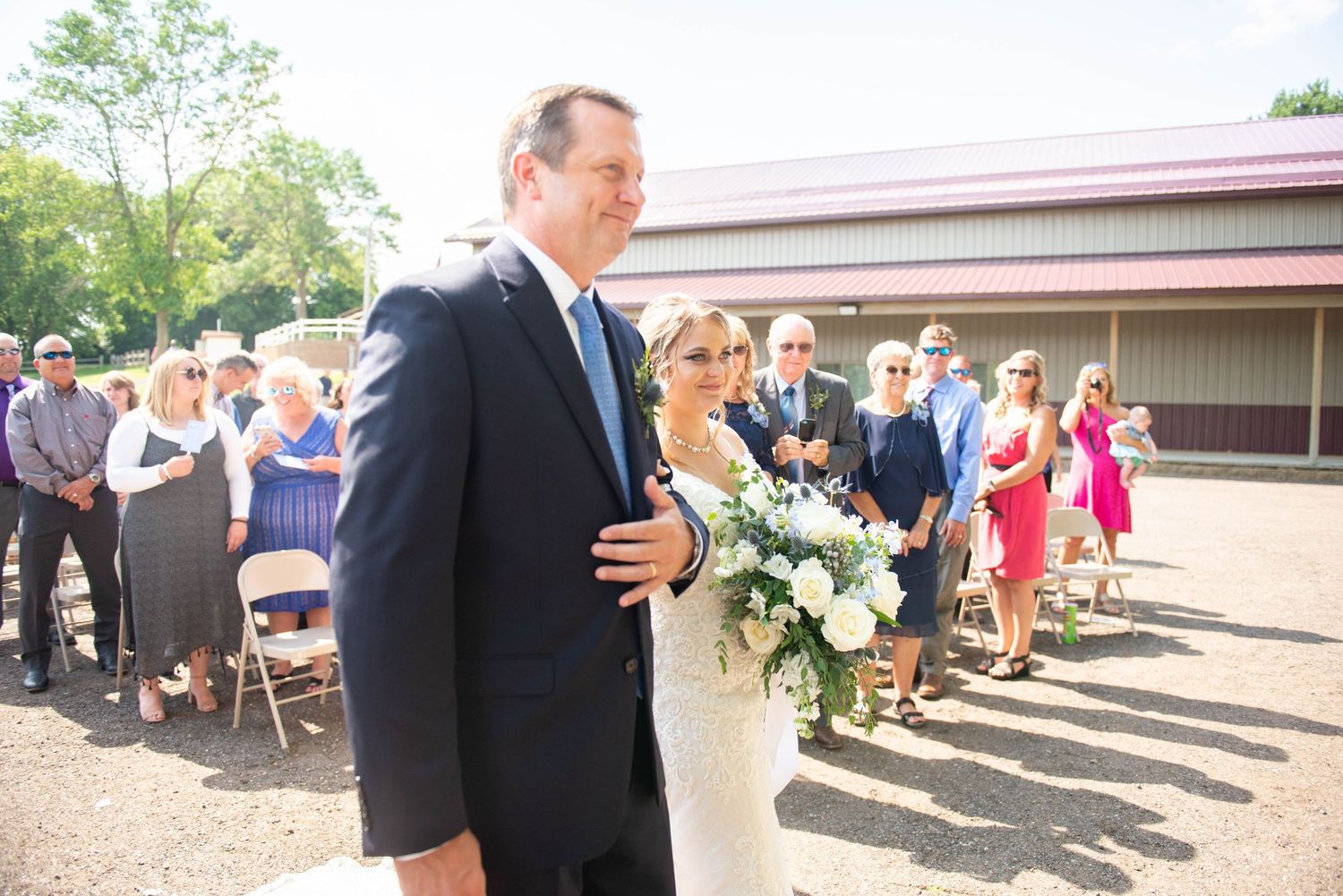 Wedding guests seated in rows during an outdoor ceremony with a building visible in the background. Zimmerman MN Weddings