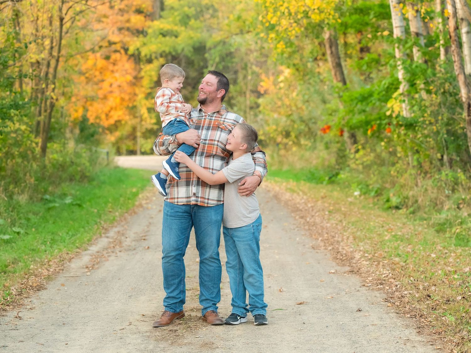 In central Minnesota a couple walks hand in hand down a leaf-covered autumn trail surrounded by colorful fall foliage. Maternity Session