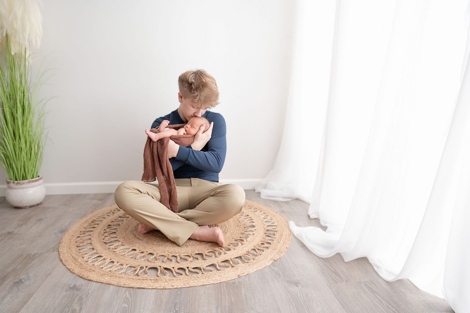 Minnesota Best newborn photographer - Sibling sitting holding baby on a round woven rug in a minimalist white room with natural light.