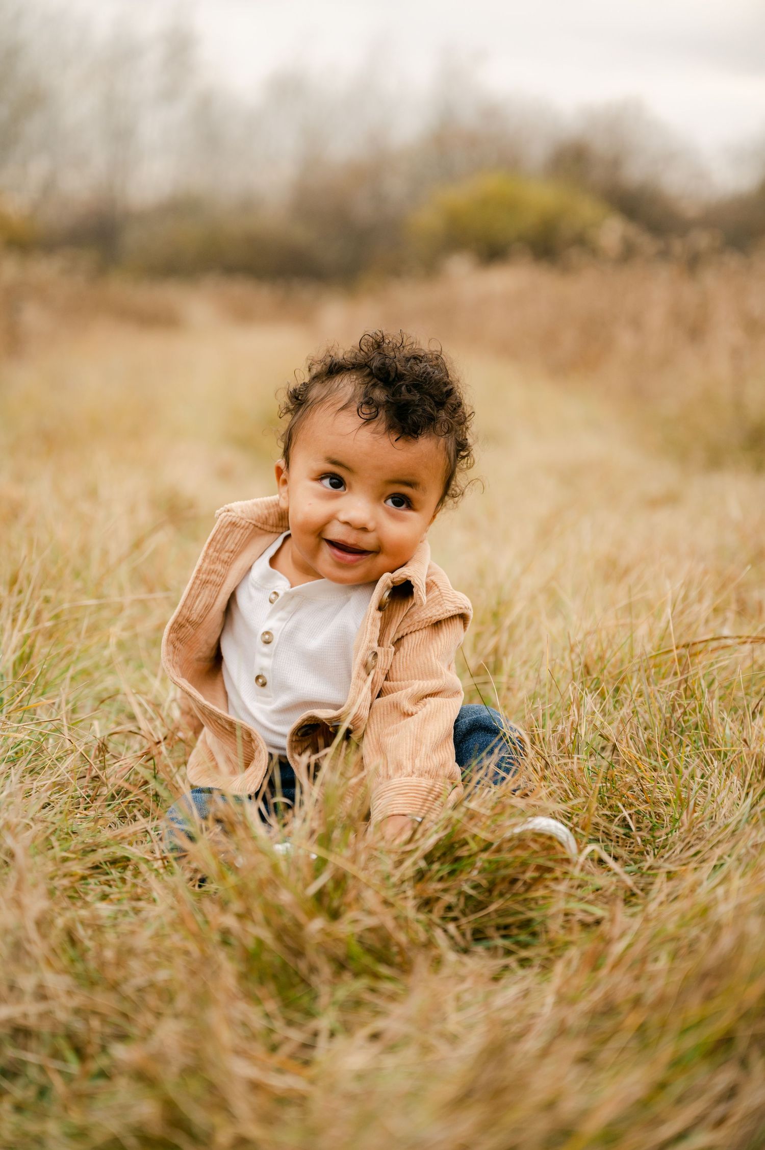 Sweet child plays peek-a-boo while sitting in a golden field of tall grass on a sunny autumn day.