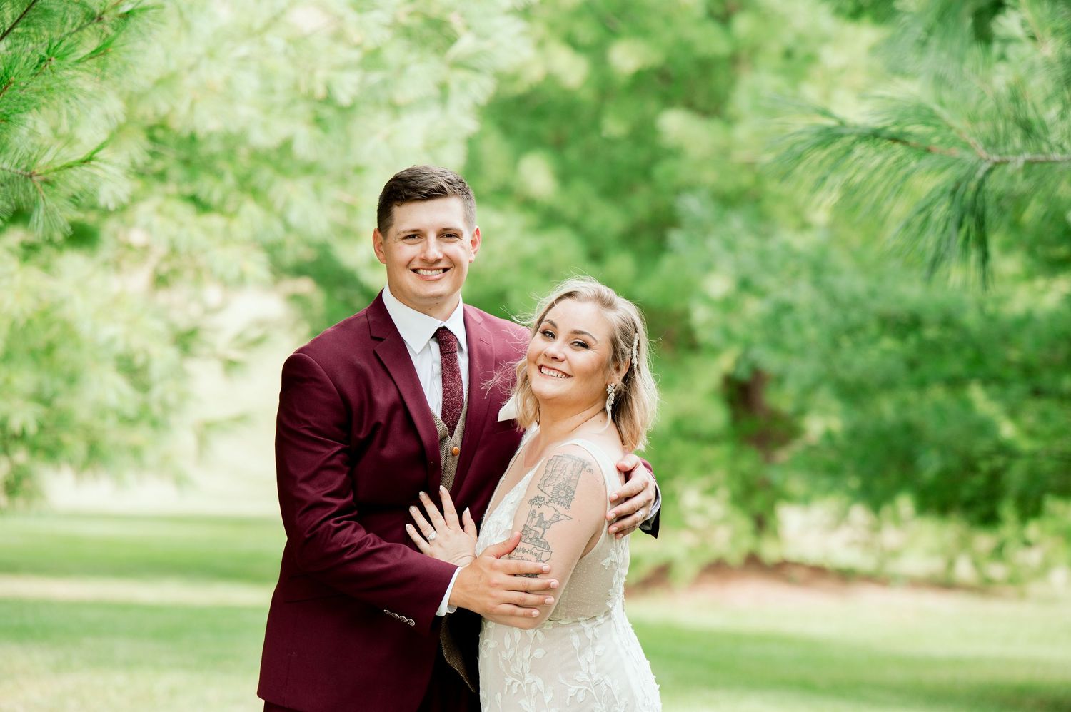 A couple in burgundy and white wedding attire share intimate moments in a garden setting.