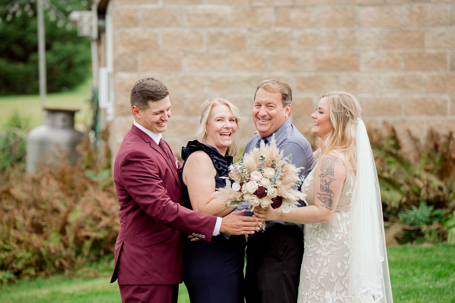 Wedding party toasts and celebrates together with champagne on a lawn by a brick building.