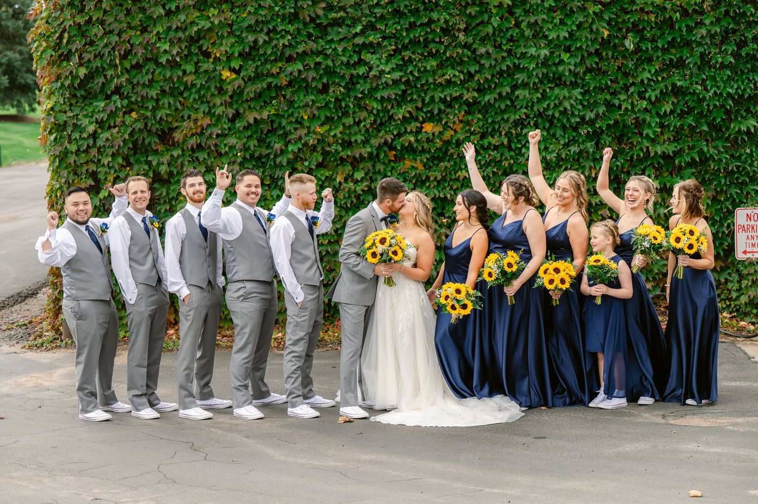 Central MN Wedding Photos | Wedding party celebrating with bride and groom kissing, bridesmaids in navy holding sunflowers.