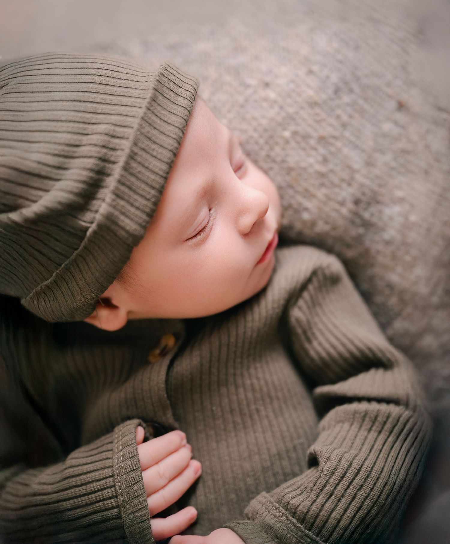 Minnesota Best newborn photographer - A sleeping baby wearing a knitted beanie and sweater rests peacefully on a textured gray surface.