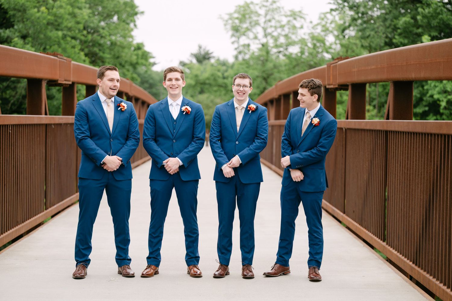 Wedding party in navy suits posing playfully on wooden bridge.