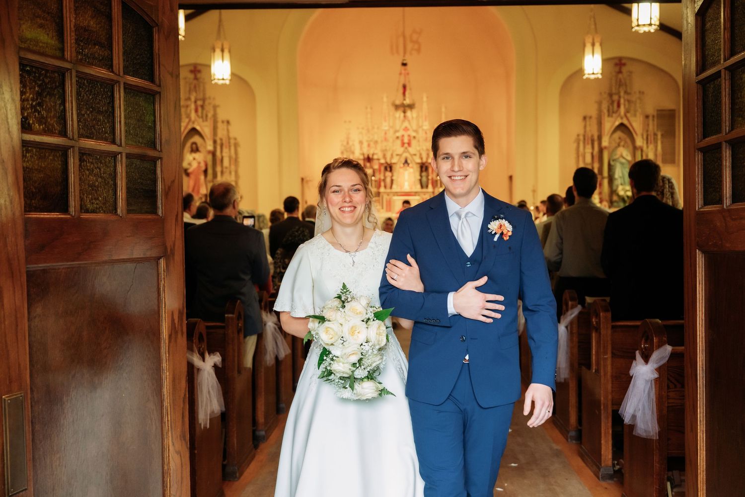 Wedding couple and guests exit a traditional church sanctuary after ceremony.
