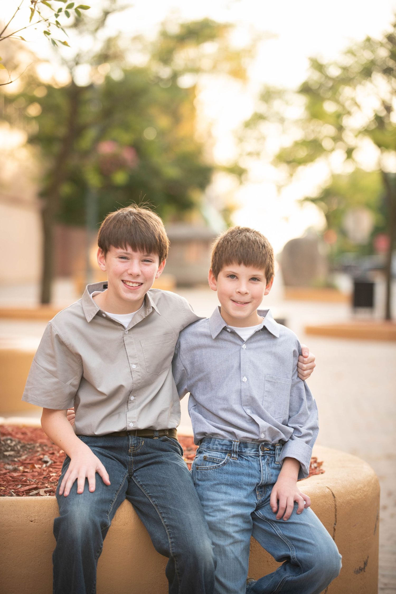 Two children in casual clothing sit together on a tan colored bench in warm sunlight.