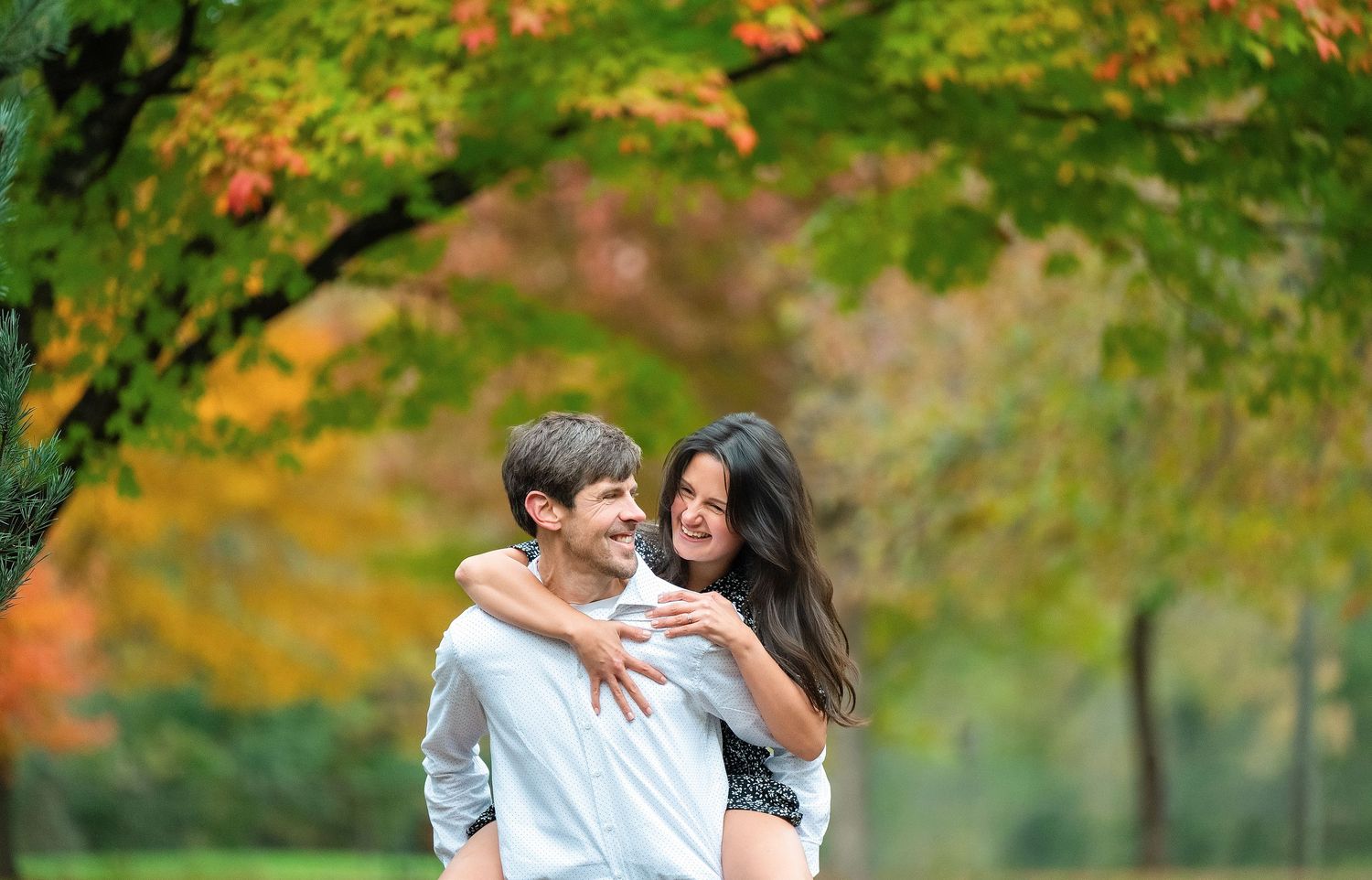 In central Minnesota a couple embraces while walking in a park with vibrant autumn foliage in the background.