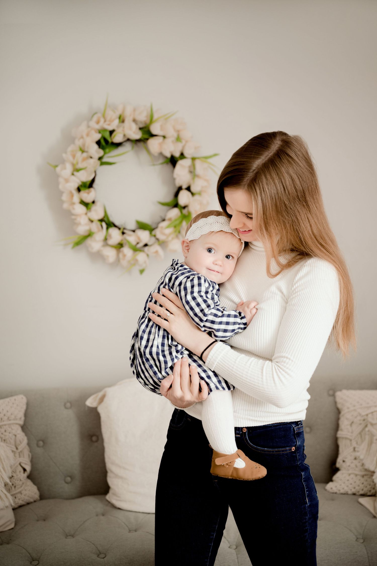 A tender moment between parent and baby against a cream wall with floral wreath decor.