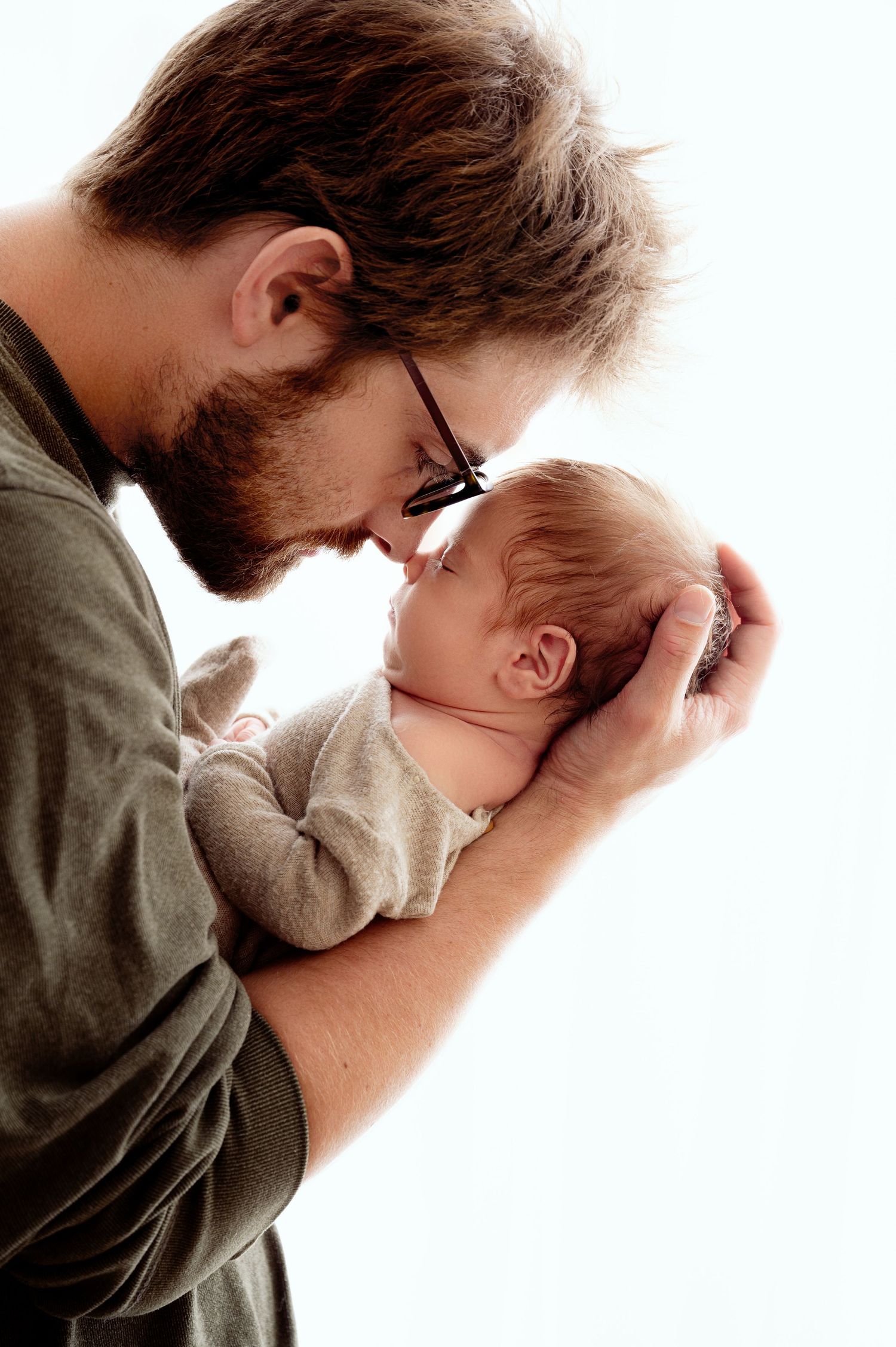 Minnesota Best newborn photographer A tender moment between a father in green shirt and a baby touching foreheads against white background.