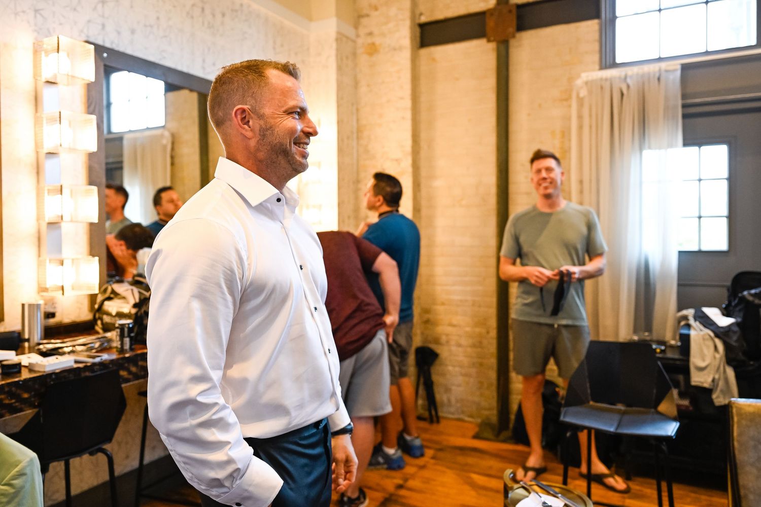 Wedding venue interior features exposed brick walls and bright windows with guests mingling.