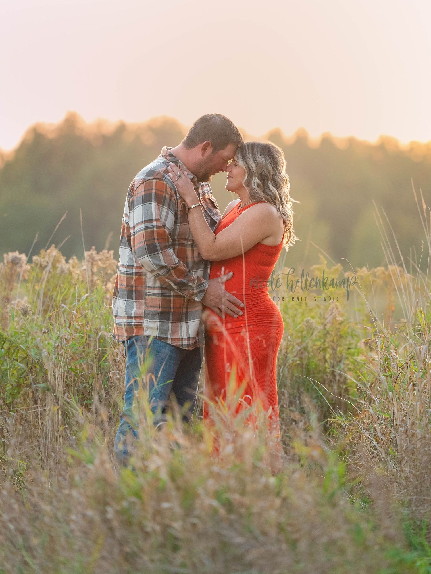A couple embraces in a golden meadow at sunset wearing plaid and coral clothing.
