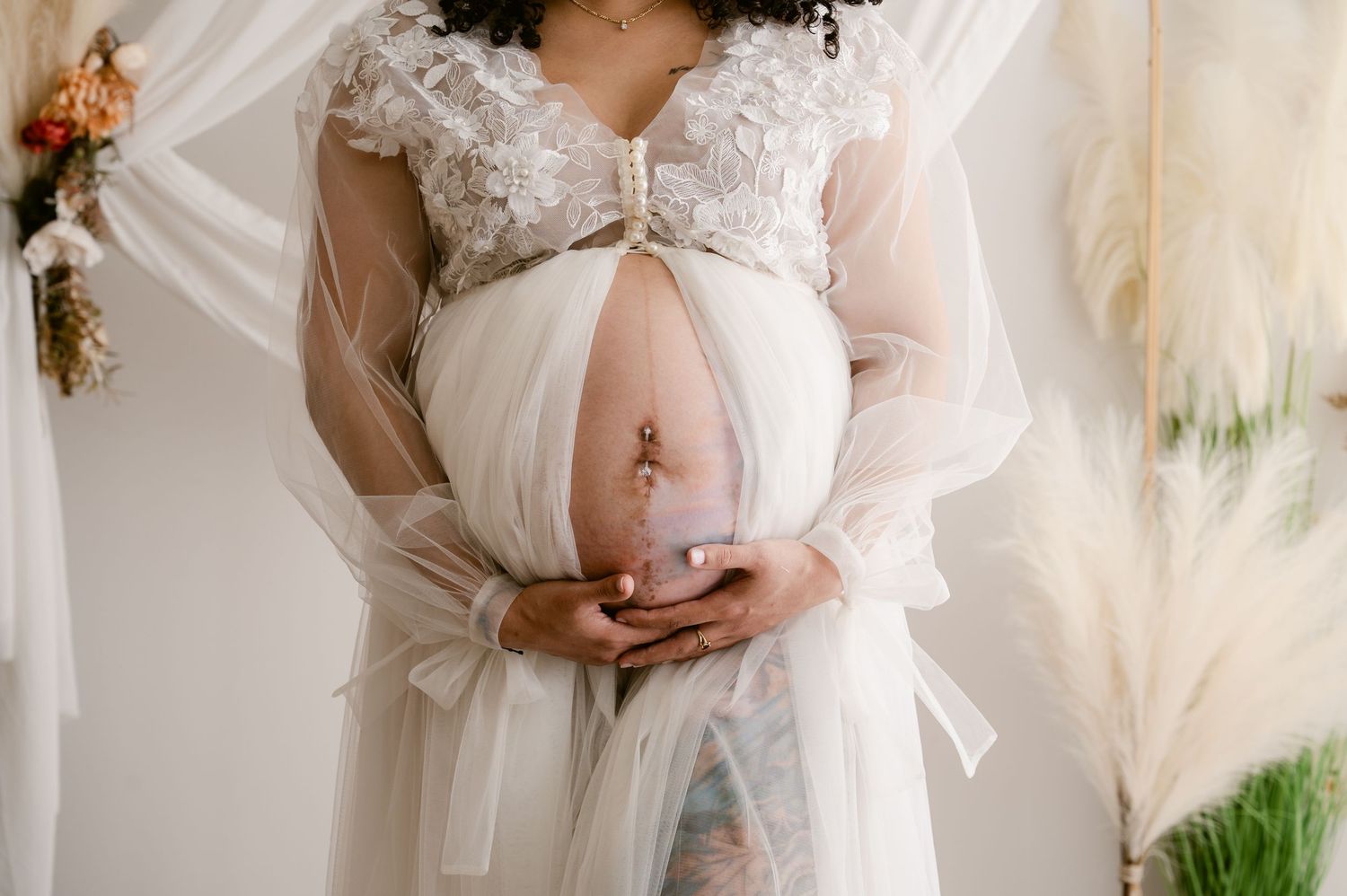 Ethereal white maternity photo session with flowing fabrics and soft natural light in a romantic indoor setting.