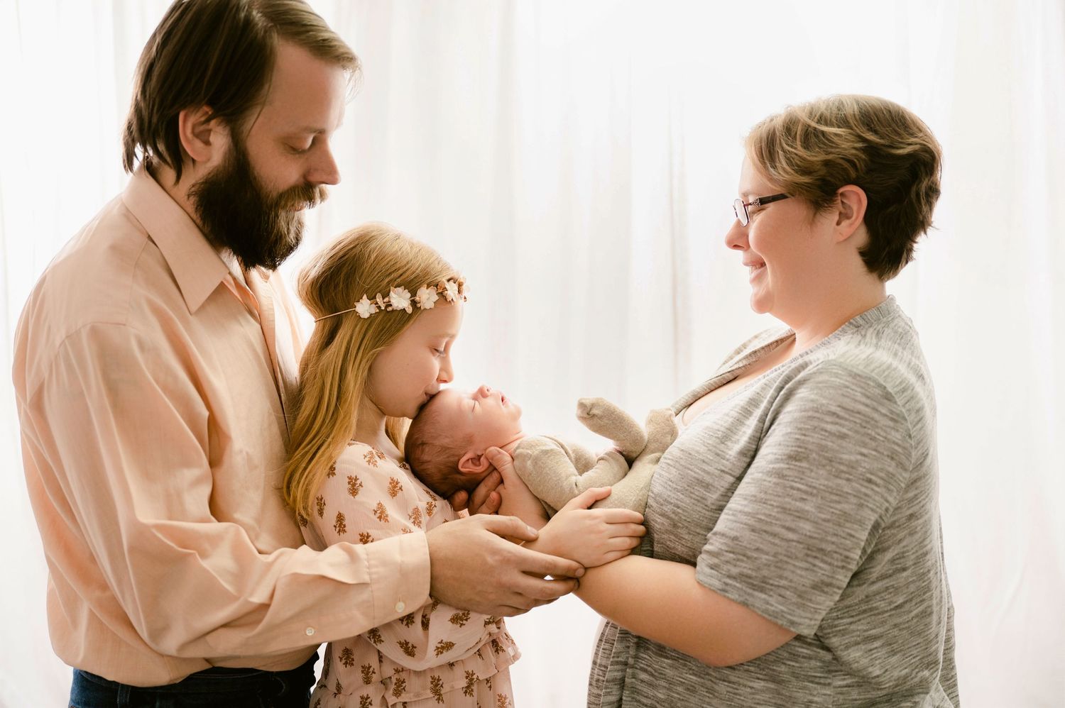Tender moments as family members take turns soothing and interacting with a small baby in a bright white room.