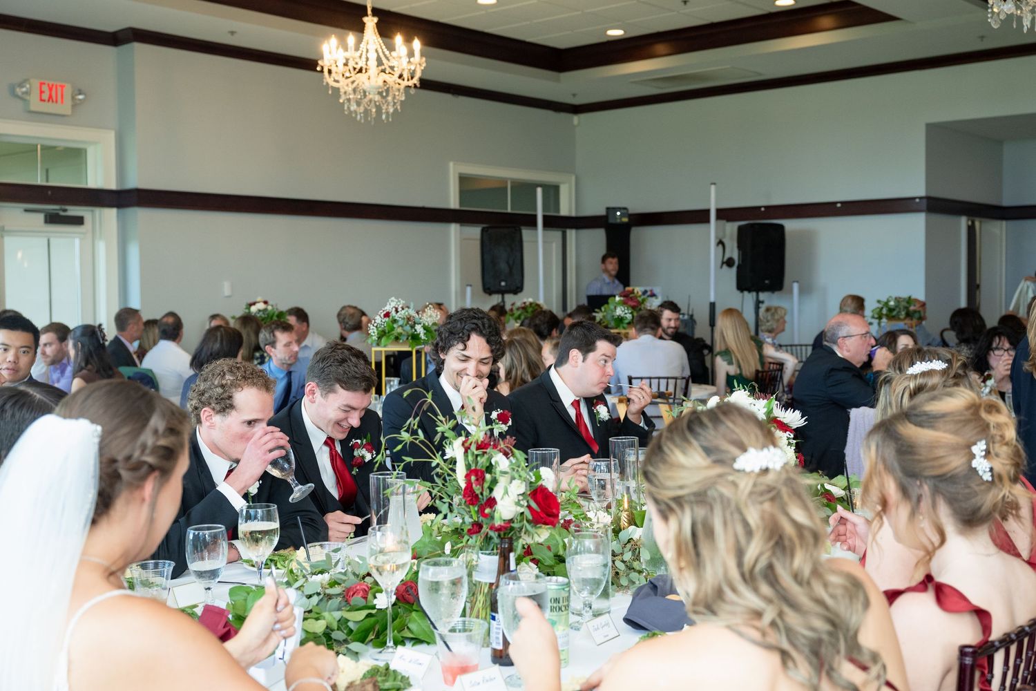 Guests celebrate at elegant wedding reception with floral centerpieces and chandelier lighting.