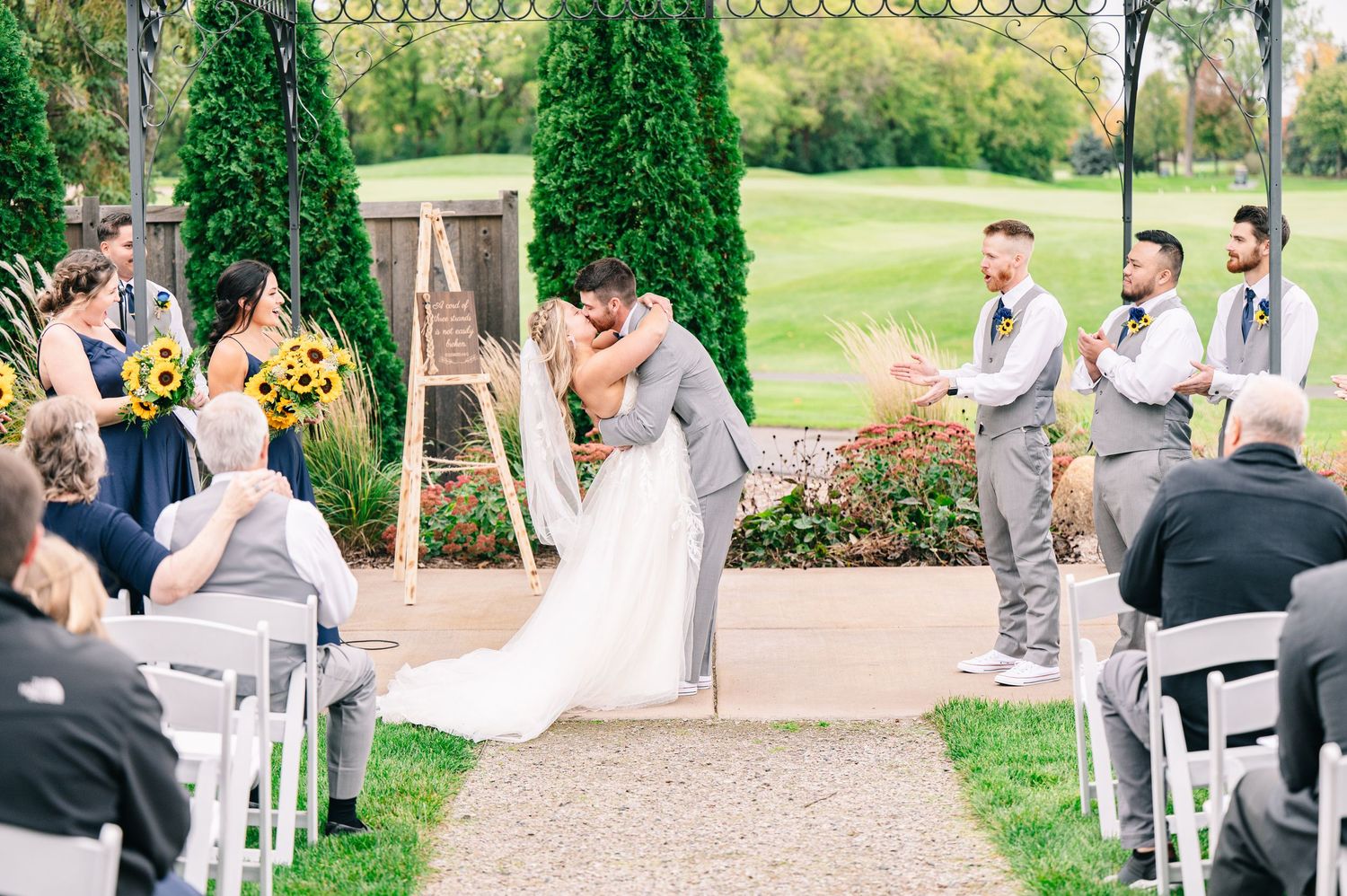 Central MN Wedding Photos - Bride and groom sharing first kiss at outdoor wedding ceremony on golf course.