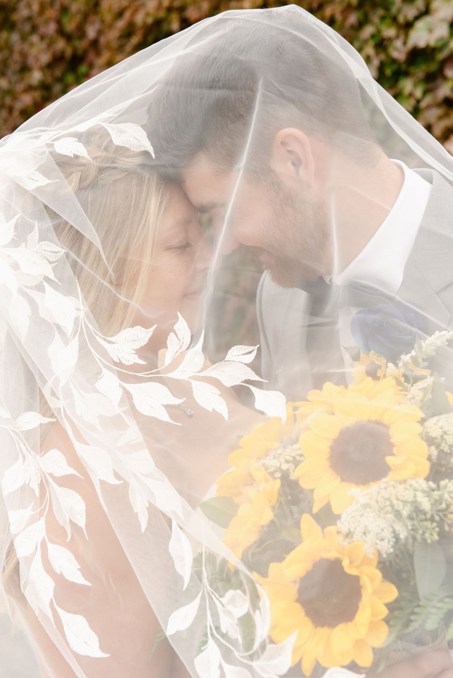 Central MN Wedding Photos | Romantic photo of bride and groom touching foreheads under a floral applique veil holding a sunflower bouquet.