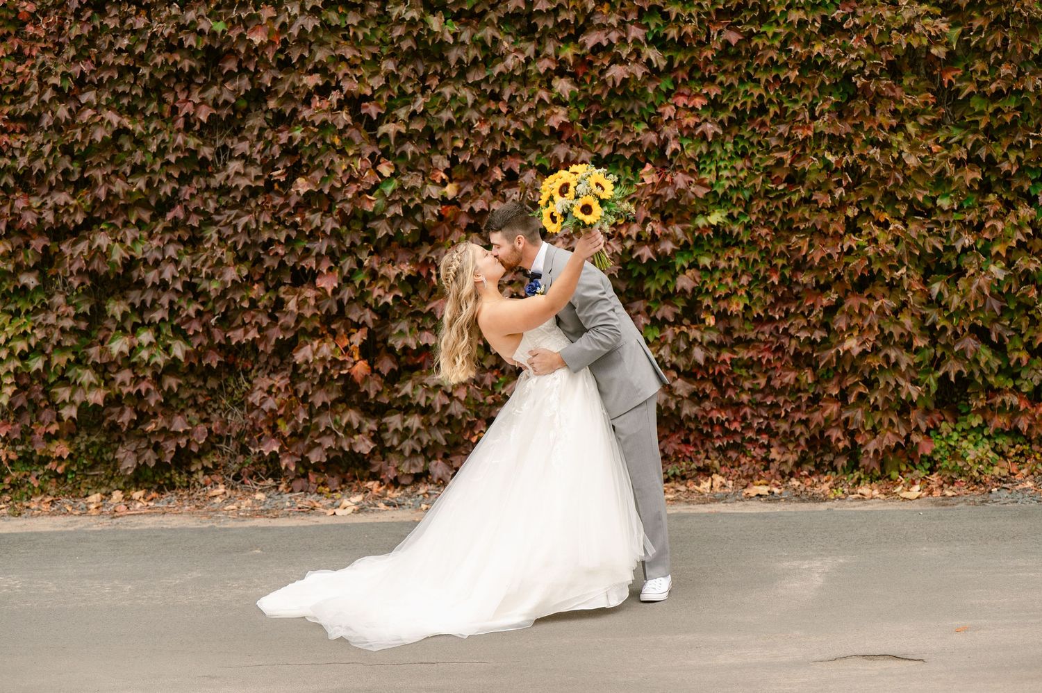 Central MN Wedding Photos | Bride and groom share a romantic kiss in front of a stunning red and green ivy-covered wall in fall.