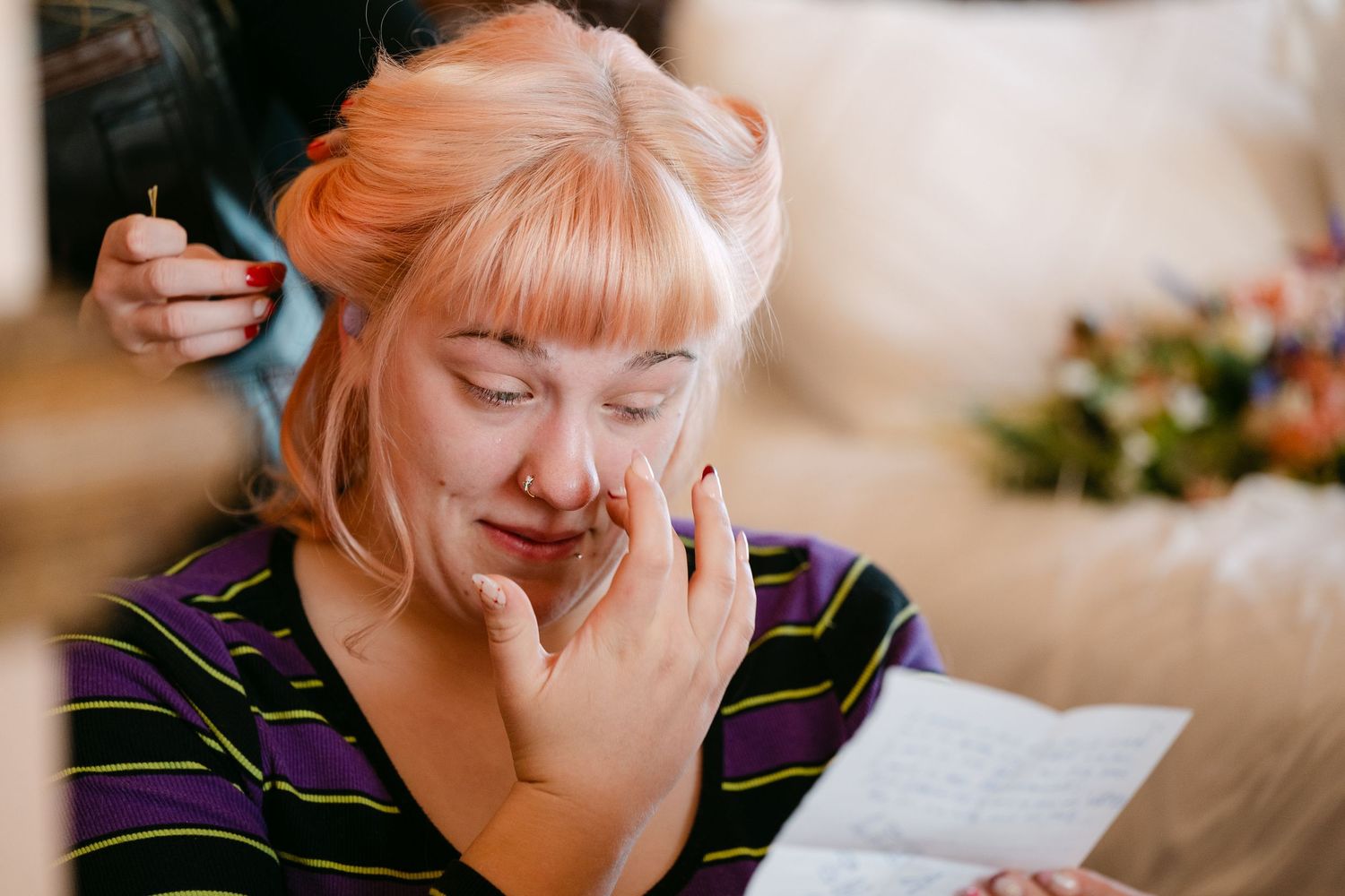 Central MN Wedding | Emotional bride crying while reading a letter during wedding preparations, with a bridesmaid styling her pink hair.