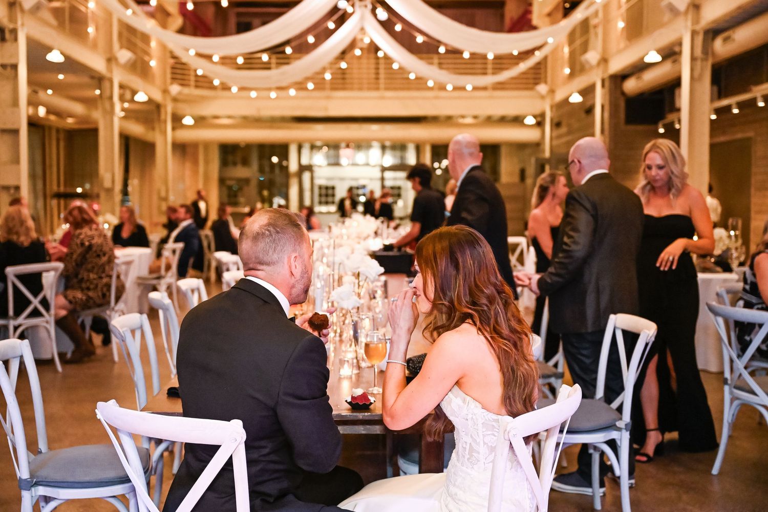 Central MN Wedding Photos | Elegant wedding reception with string lights, guests at decorated tables, bride and groom seated in foreground