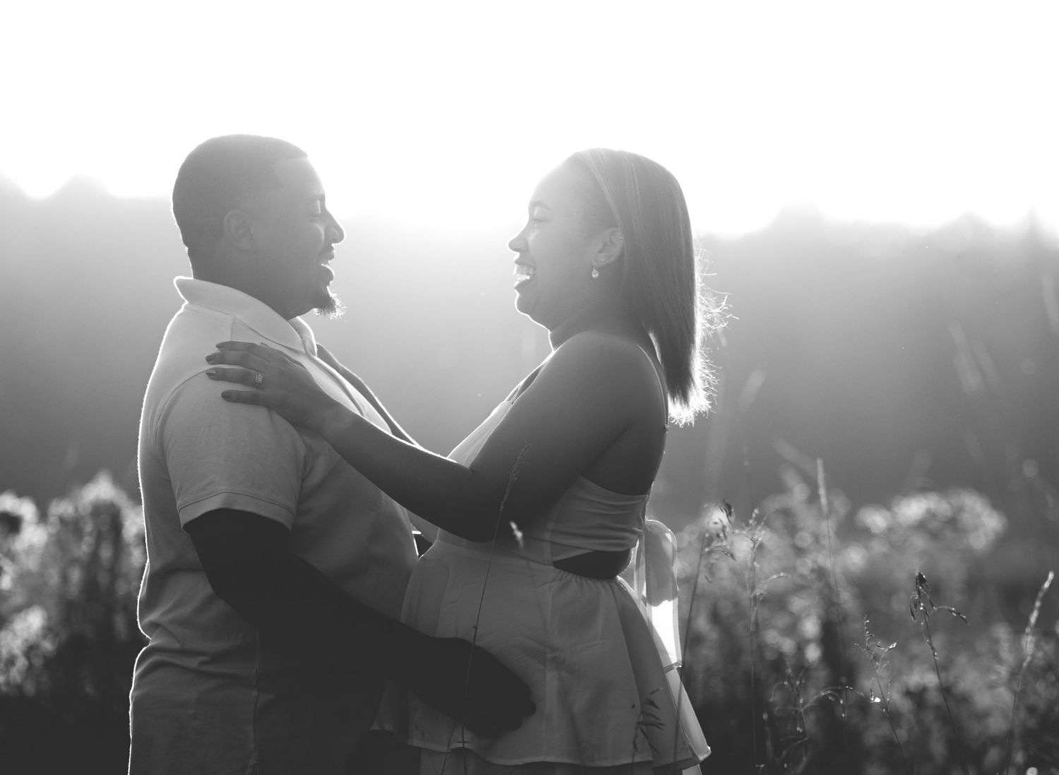 Central Minnesota Best Engagement Photos - Black and white photo of a couple embracing and smiling at each other outdoors in a sunlit field.