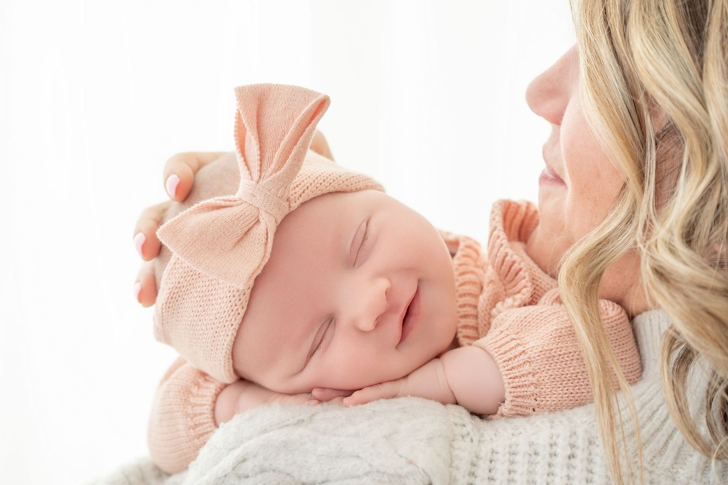 Minnesota Best newborn photographer Baby wearing pink knit sweater and matching bow headband lies on white blanket in delicate newborn pose.