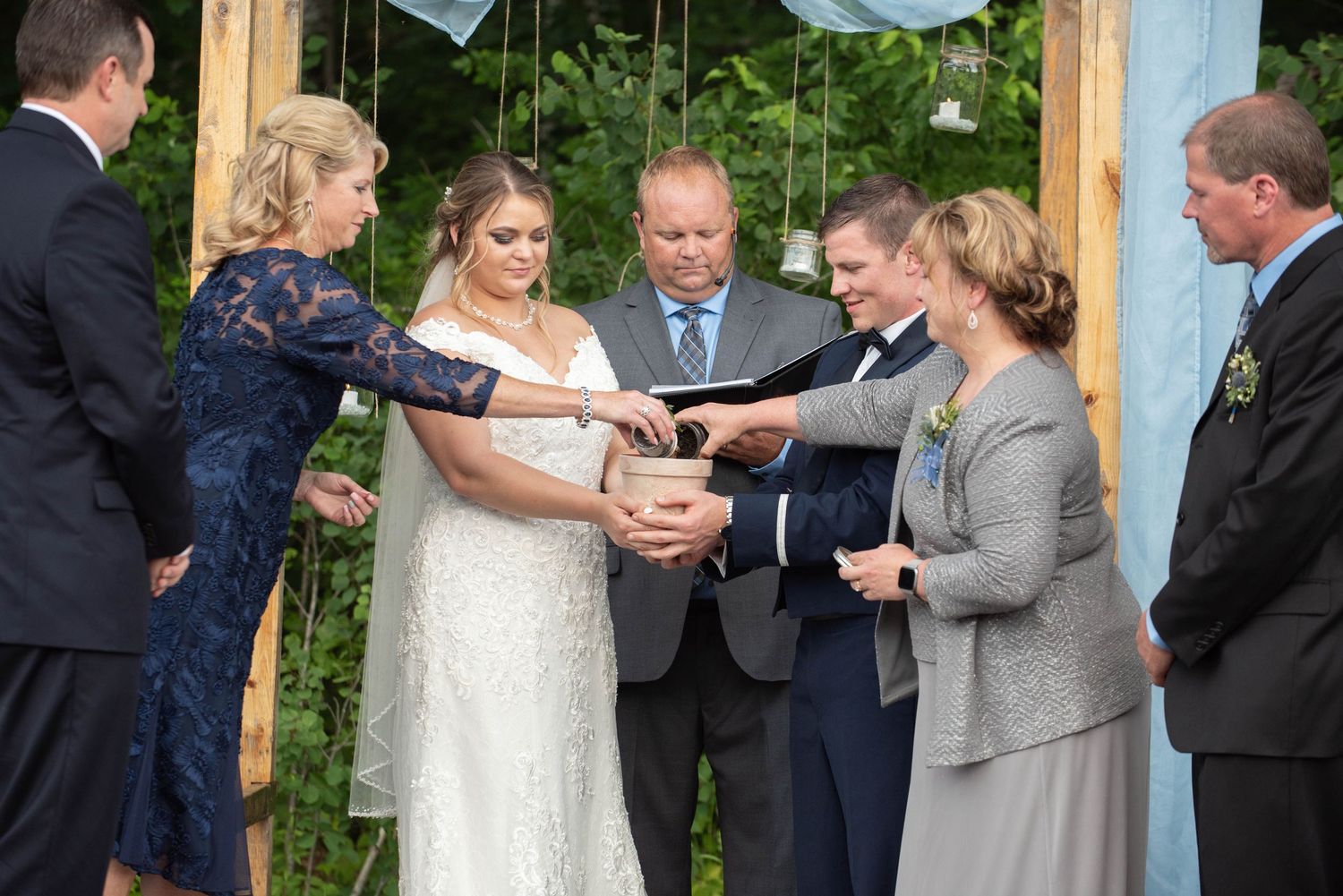 Wedding exchange taking place beneath rustic wooden posts decorated with white fabric outdoors. Zimmerman MN Weddings