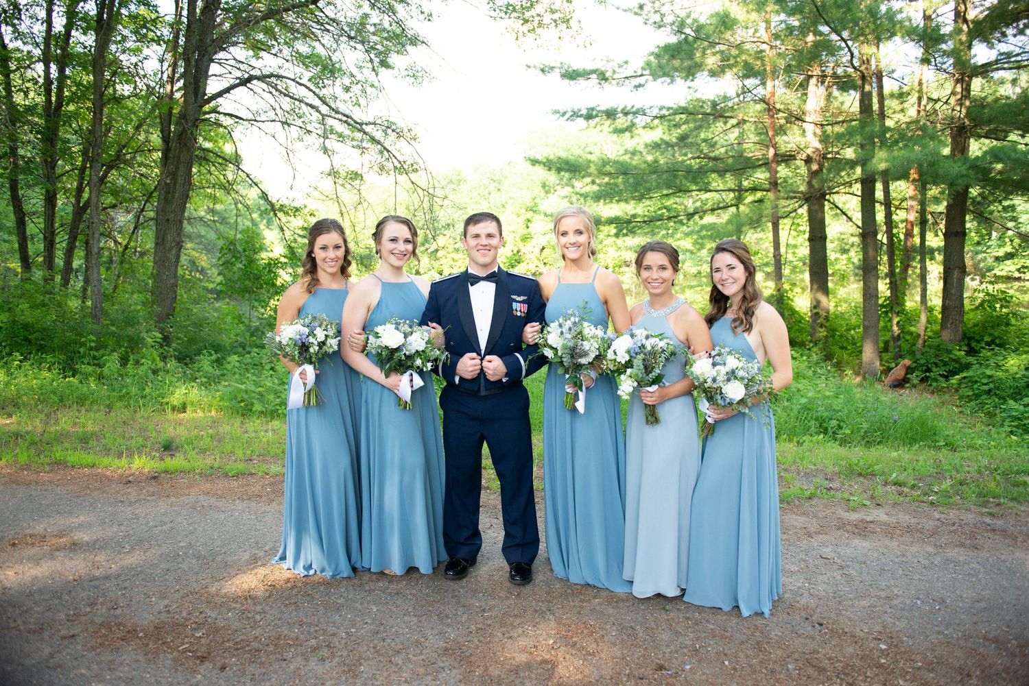 Wedding party poses in blue dresses and formal attire on a forest path during golden hour. Zimmerman MN Weddings