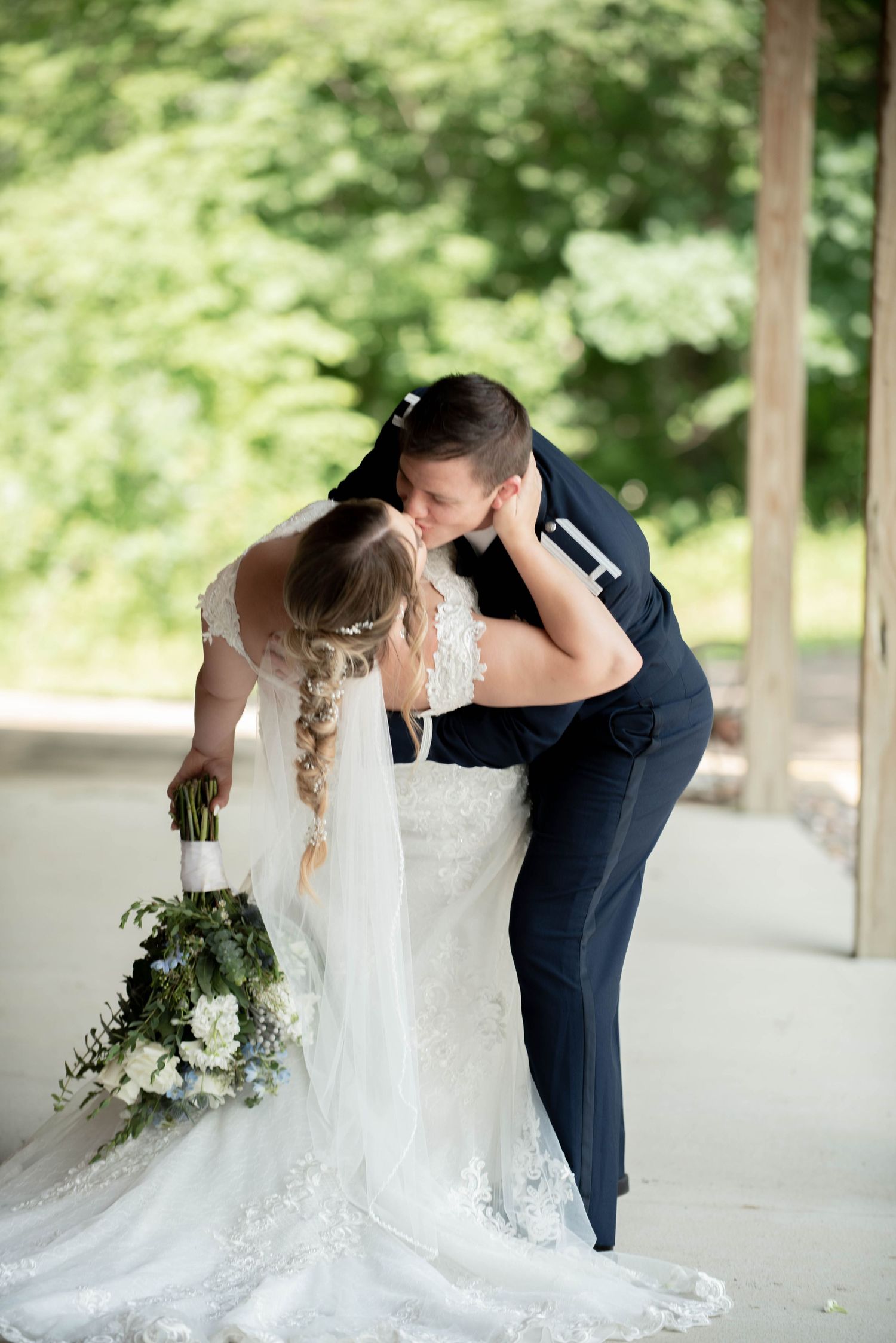A romantic wedding moment with the couple in an intimate pose, with a white lace dress and navy suit under a covered porch. Zimmerman MN Wed