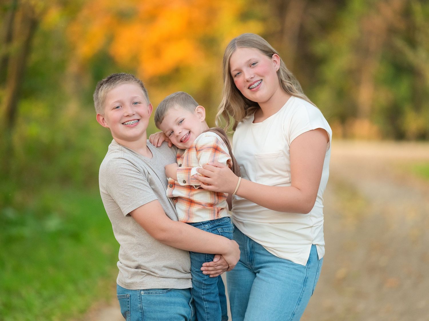 Family wearing casual outfits poses together on a dirt path surrounded by autumn foliage.