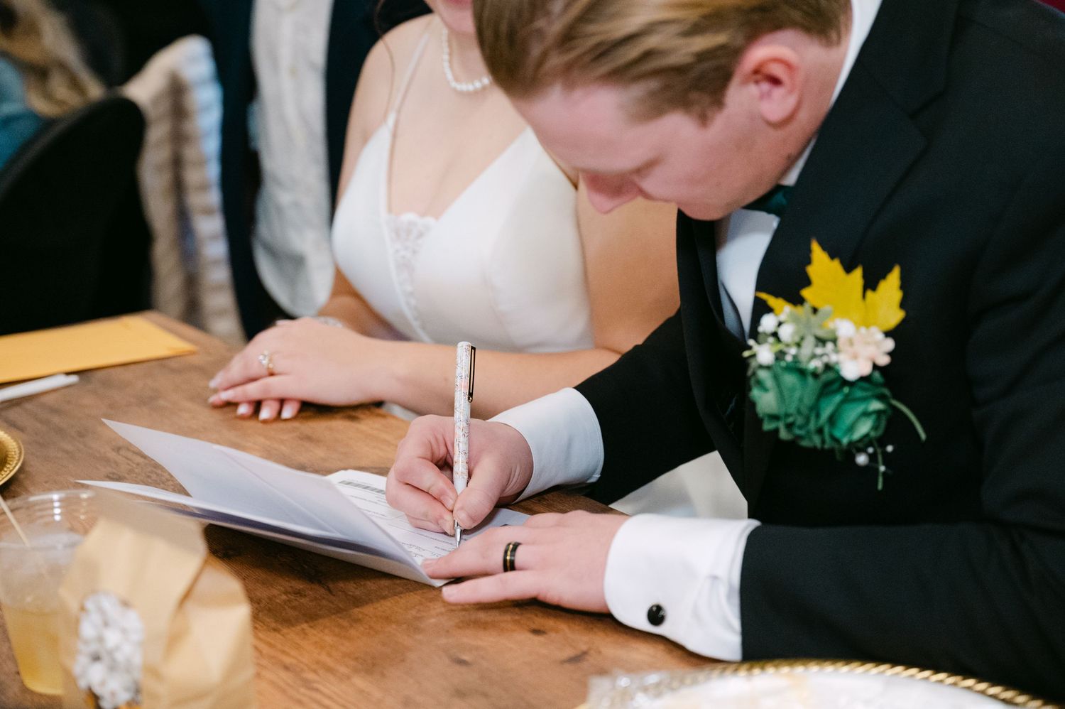 Signing a marriage certificate during a wedding ceremony while wearing formal black and white attire.