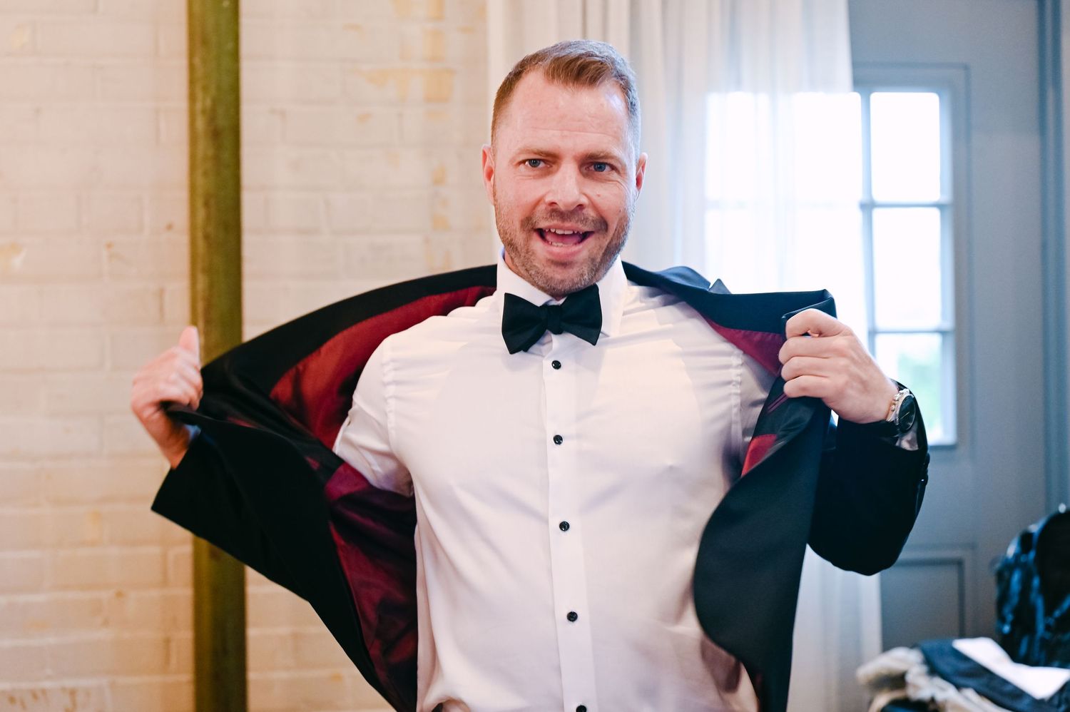 Person adjusting bowtie while wearing formal black tuxedo in preparation for event.