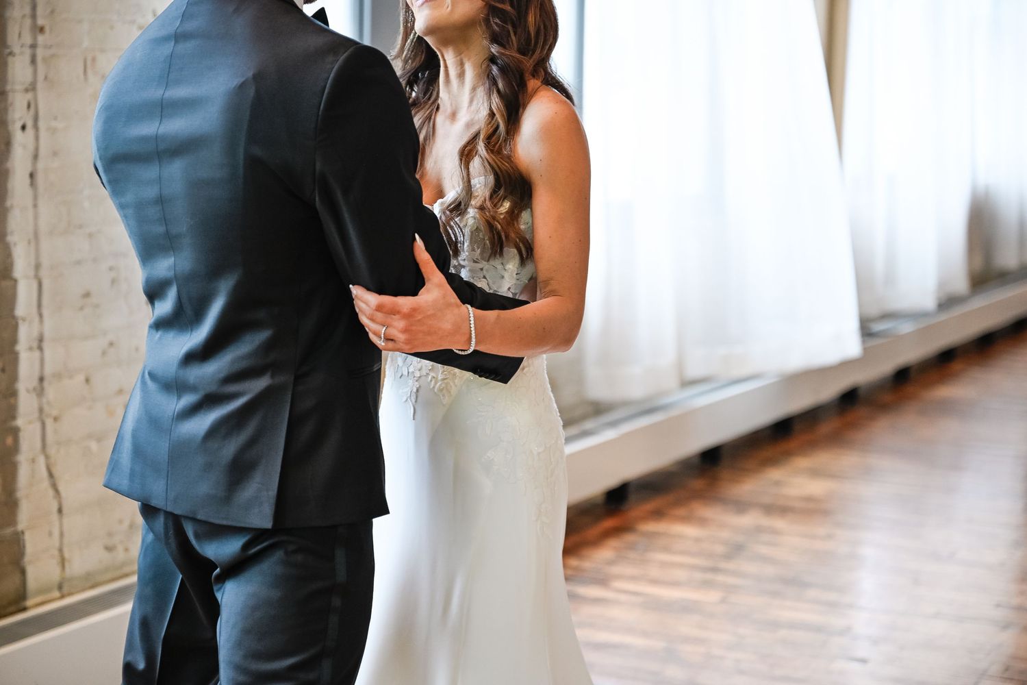 Couple shares emotional first look moment in bright sunlit room with white curtains.