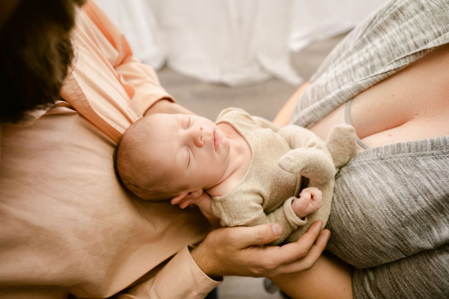 A sleeping baby in cozy clothing grasps a small plush toy while resting on soft fabrics.