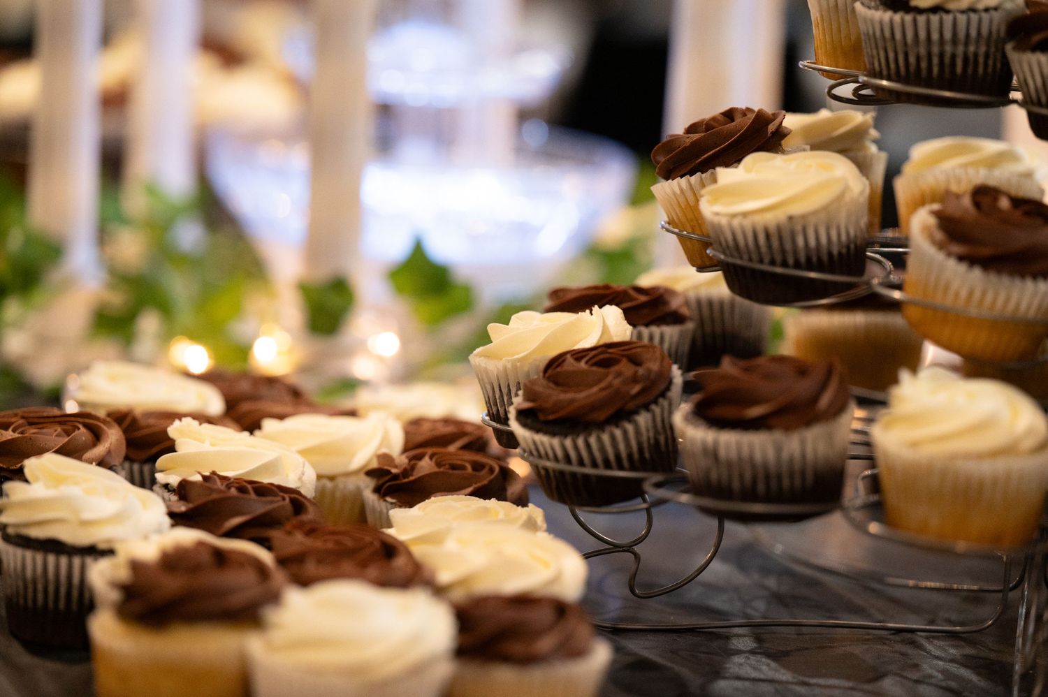 Chocolate and vanilla cupcakes with frosting arranged on decorative display stands at a wedding reception.