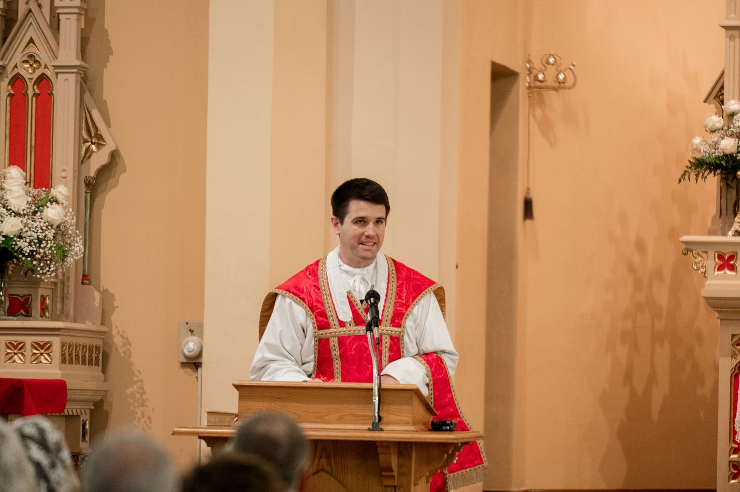 Person in red and white religious vestments speaking at church altar during ceremony.